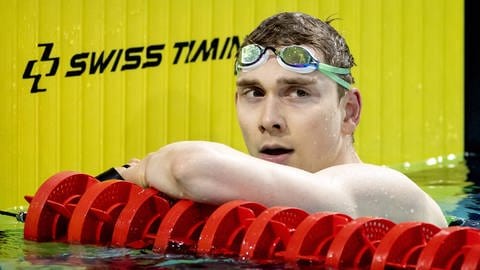 Olympia-Schwimmer Henning Mühlleitner lehnt mit seinem linken Arm auf dem roten Bahnentrenner und hat sich die Schwimm-Brille auf die Stirn gezogen.