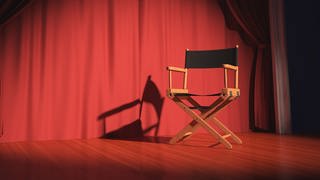 Ein Regiestuhl auf einer Bühne mit rotem Vorhang (Foto: Colourbox)