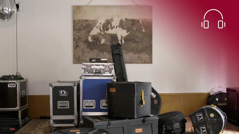 Foto zum Dokumentarfilm Haldern Pop - Dorf mit Festival: Cases und weiteres Musikequipment in der Haldern Pop Bar, im Hintergrund ein großes Bild mit einer Kuh, rotes Overlay mit Icon Kopfhörer (Foto: SWR, Monika Pirch Filmproduktion, Stefanie Gartmann)