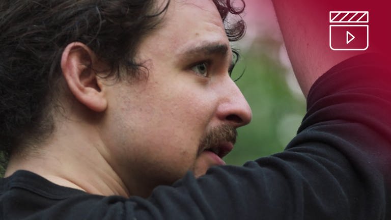 Standbild aus dem Dokumentarfilm Endlich Tacheles: Yaar beim Schwertkampf, rotes Overlay mit Icon Filmklappe (Foto: SWR, HANFGARN & UFER, Lars Barthel)