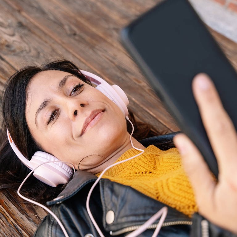 SWR1 zum Hören, wann und wo Sie wollen (Foto: Frau mit Kopfhörern und Smartphone liegt auf dem Holzboden) (Foto: IMAGO, IMAGO / Addictive Stock)