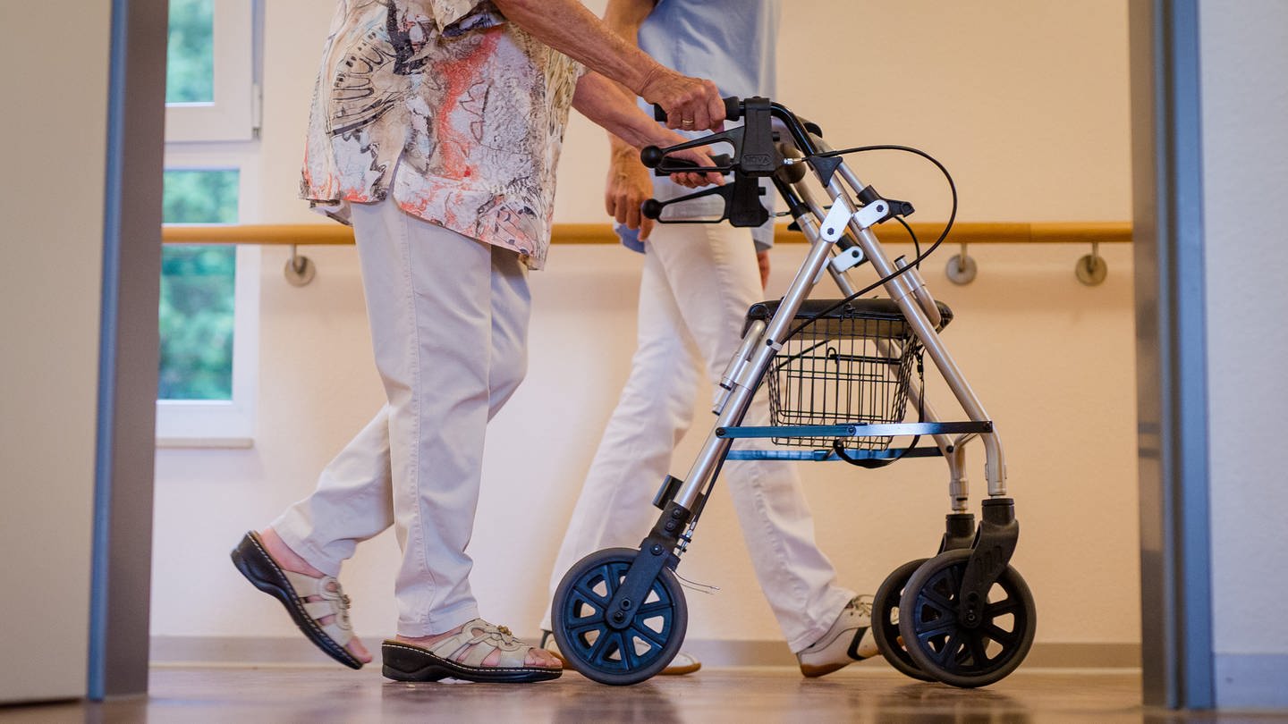 Eine Pflegekraft geht in einem Pflegeheim mit einer älteren Dame über einen Korridor. Debatte kinderlose müssen mehr in die Pflegeversicherung einzahlen (Foto: picture-alliance / Reportdienste, Picture Alliance)