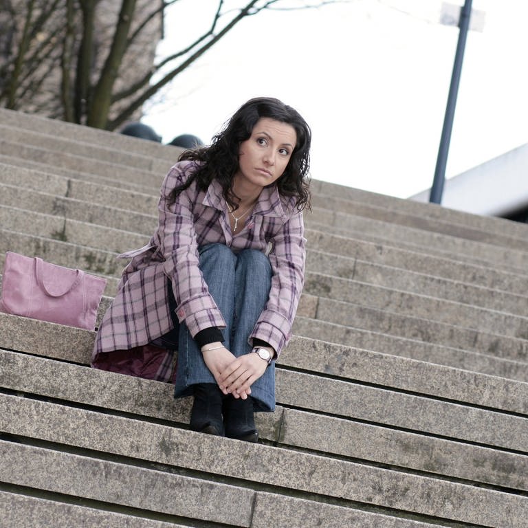 Junge Frau sitzt gelangweilt auf einer Treppe.