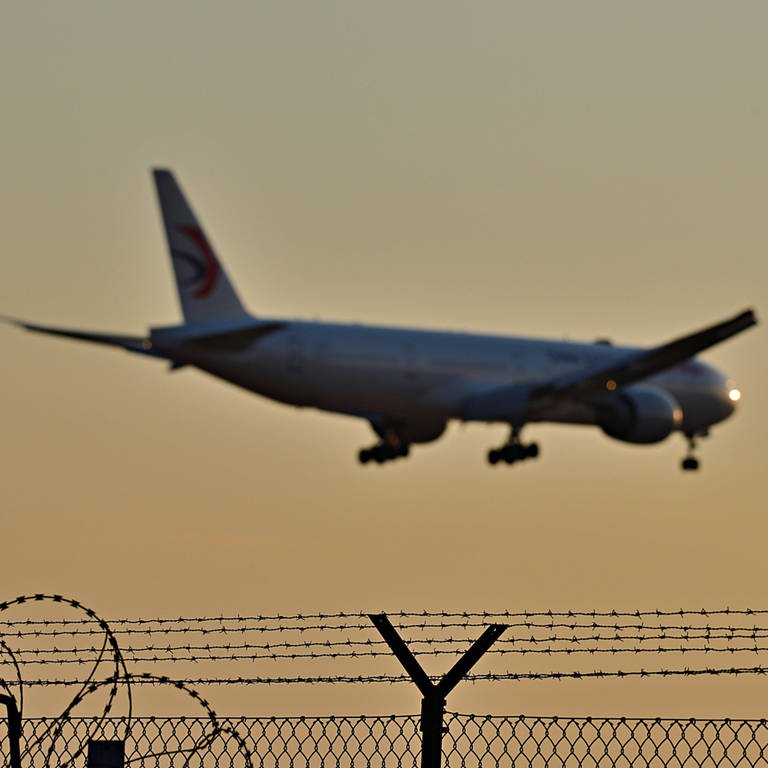 Asyl und Abschottung Stacheldrahtbewehrte Zäune, darüber ein Flugzeug (Foto: IMAGO, imago images)