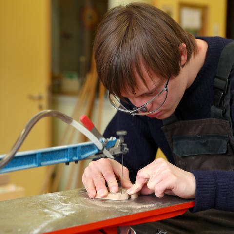 Philipp, ein Jugendlicher mit Down-Syndrom, arbeitet an der Dekupiersäge in der Holzwerkstatt der Goldbach Werkstatt Nürnberg, eine Werkstatt für Menschen mit Behinderung. 