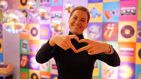 SWR1 Moderatorin Cora Klausnitzer formt ein Herz mit ihren Händen und schickt Liebe an alle SWR1 Hitparade-Fans. (Foto: SWR)