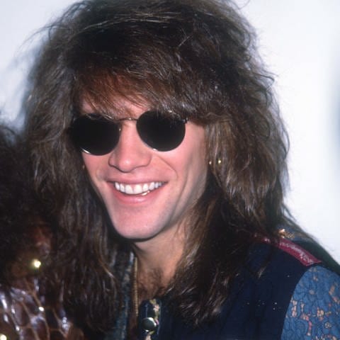 Jon Bon Jovi steht 1990 auf einer Bühne mit einem Mikrofon in der Hand und fordert das Publikum auf, zu singen. (Foto: picture-alliance / Reportdienste, newscom)