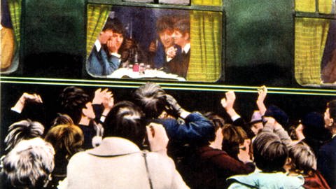 Die Beatles sitzen im Zug und sind durchs Fenster sichtbar. Vor dem Zug viele Fans. (Foto: IMAGO, imago images/Everett Collection)
