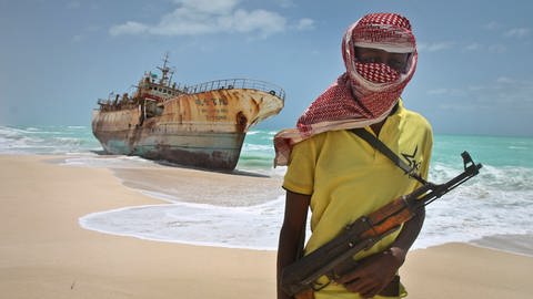 Ein somalischer Pirat steht vor einem rostigen Schiffswrack und hält eine Pistole in der Hand. (Foto: picture-alliance / Reportdienste, Picture Alliance)