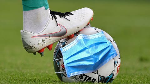 Mundschutzmaske bedeckt einen Fußball (Foto: dpa Bildfunk, Sven Simon)