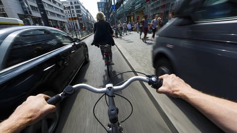 Ein Radfahrer wird im Stadtverkehr von einem nah vorbeifahrenden Auto überholt. (Foto: IMAGO, imago/photothek)