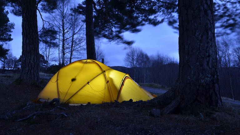 Gelb erleuchtetes Expeditionszelt, unter großen Bäumen, Abendstimmung. (Foto: picture-alliance / Reportdienste, Picture Alliance)