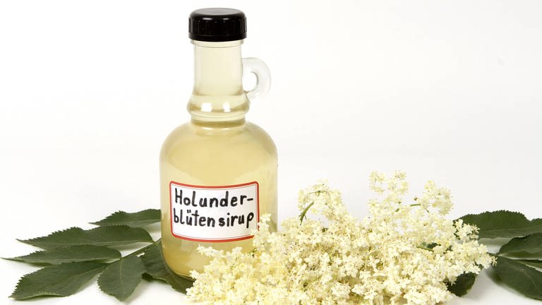 Eine kleine Flasche Holundersirup, davor liegen Holunderblüten. (Foto: IMAGO, imago/CHROMORANGE)
