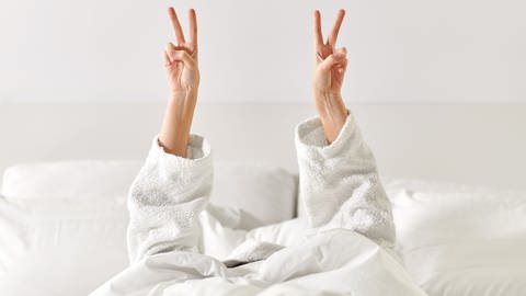 Eine im Bett liegende Person streckt beide Hände nach oben und macht das "Peace"-Zeichen. (Foto: picture-alliance / Reportdienste, picture alliance / Zoonar | lev dolgachov)