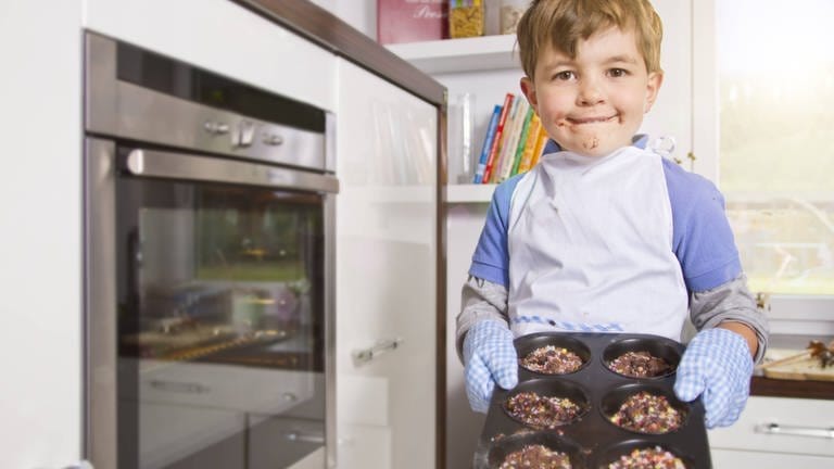 Ein kleiner Junge steht mir selbstgebackenenen Muffins vor dem Backofen (Foto: IMAGO, imago stock&people)