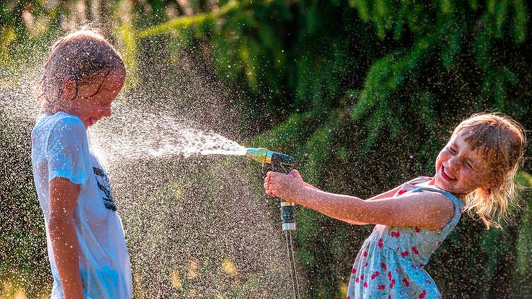 Abkühlung im Sommer: ein Mädchen bespritzt einen Jungen mit Wasser aus dem Gartenschlauch, beide lachen und freuen sich (Foto: picture-alliance / Reportdienste, picture alliance/dpa/dpa-Zentralbild | Jens Büttner)