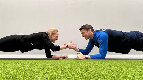 Der Athletiktrainer des SC Freiburg, Daniel Wolf, gibt SWR1 Moderation Laura Zacharis Trainingstipps. Gegenüber auf dem Boden klatschen sie sich ab. (Foto: SWR)