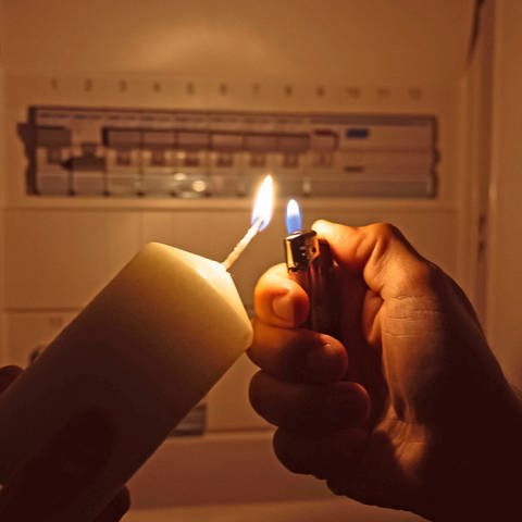 Stromausfall: ein Mann zündet mit einem Feuerzeug eine Kerze an, dahinter sieht man einen Sicherungskasten - die Sicherungen sind offensichtlich alle in "An"-Stellung (Foto: picture-alliance / Reportdienste, picture alliance / CHROMORANGE | Michael Bihlmayer)