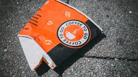 Ein Einwegbecher für Kaffee liegt auf dem Boden. Die Plastikbeschichtung aus Polyethylen zersetzt sich mit der Zeit zu kleinen Plastikpartikeln - Mikroplastik. Dieses ist eine Belastung für Böden, Gewässer und Tiere. (Foto: picture-alliance / Reportdienste, picture alliance | Christian Ohde)