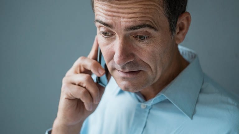 Ein Mann telefoniert mit einem Handy und schaut besorgt. Betrüger versuchen durch Schockanrufe Menschen um ihr Geld zu bringen. (Foto: picture-alliance / Reportdienste, picture alliance / Westend61 | Joseffson)