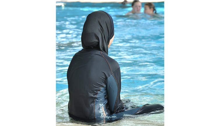Anderer Glaube, andere Sitten: Eine muslimische Schülerin sitzt im Westbad in Freiburg in einem Burkini am Rande des Schwimmbeckens. Immer wieder gab es Versuche, Burkinis in Schwimmbädern zu verbieten - doch Gerichte schmetterten diese immer ab. Das Burkini-Verbot verstoße gegen das verfassungsrechtliche Gleichbehandlungsgebot. (Foto: picture-alliance / Reportdienste, Picture Alliance)