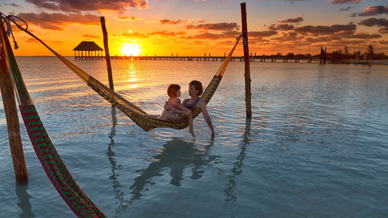 Mutter und Kind in Netzhängematte über Meer bei Sonnenuntergang (Foto: IMAGO, -)