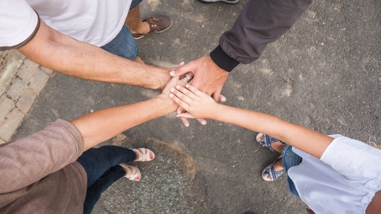 Eine Familie legt die Hände in der Mitte aufeinander. (Foto: IMAGO, Simona Pilolla)
