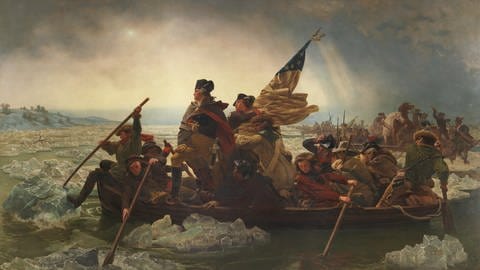 Auf dem Gemälde ist Washington in einem Boot zusammen mit seinen anderen Männern zu sehen. Sie tragen Flaggen und steuern das Ufer an. Im Hintergrund sind weitere Boote zu sehen. (Foto: dpa Bildfunk, Picture Alliance)