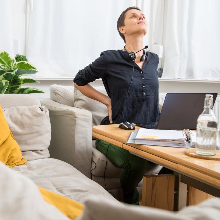 HomeOffice: Frau arbeitet vom Sofa aus am Computer und hat Rückenschmerzen (Foto: picture-alliance / Reportdienste, Christin Klose)