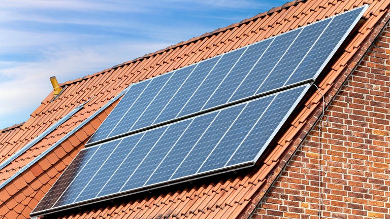 Eine Solaranlage auf dem Dach eines älteren Privathauses mit roten Klinkersteinen sorgt für sauberen, umweltfreundlichen Strom.