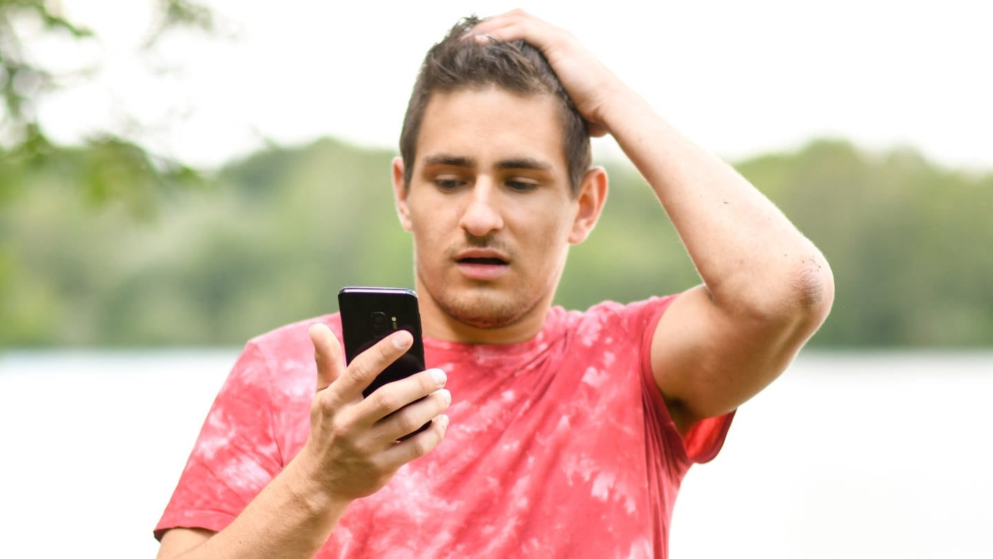 Junger Mann schaut erschreckt auf sein Handy (Foto: picture-alliance / Reportdienste, picture alliance / dpa Themendienst | Tobias Hase)