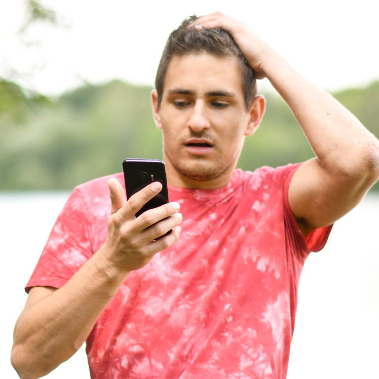Junger Mann schaut erschreckt auf sein Handy