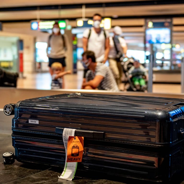 Eine Familie wartet am Gepäckband eines Flughafens auf ihren Koffer.