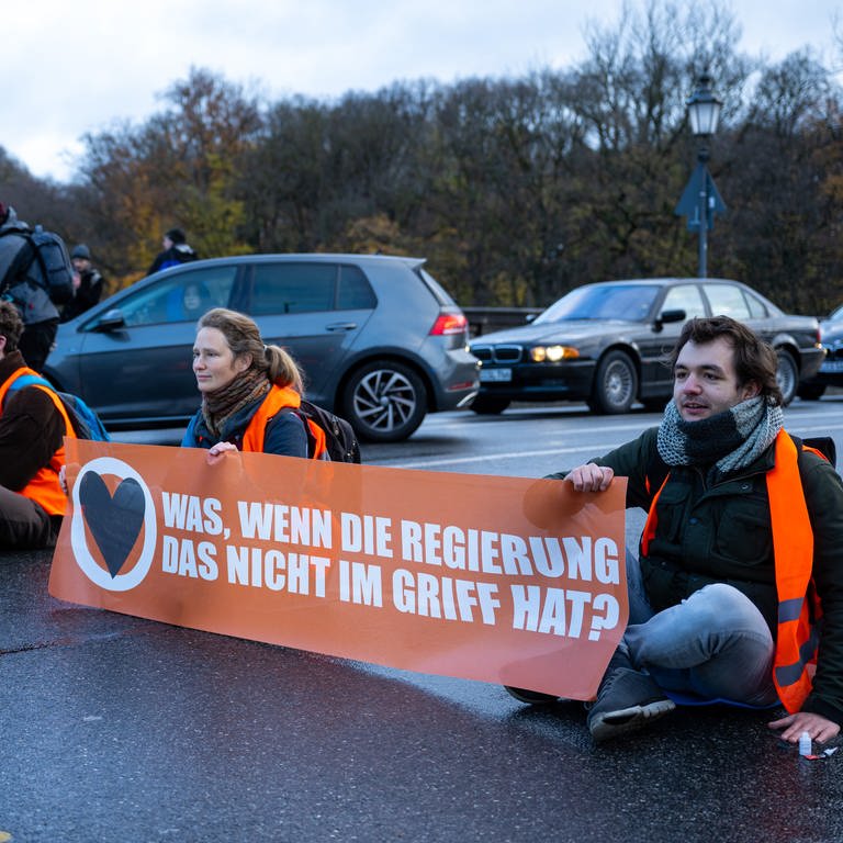 Klimaaktivisten der Umweltschutzbewegung "Letzte Generation" sitzen auf einer Straße und blockieren den Verkehr.