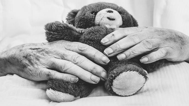 Fotowerk von Andy Reiner: Hände eines alten Menschen, die einen Teddybären halten.