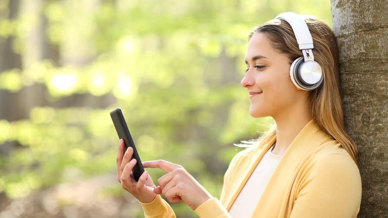 Junge Frau hört Musik über ihr Smartphone und hat Kopfhörer auf.