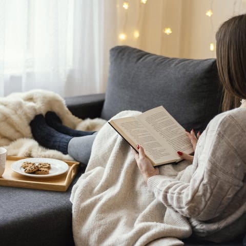 Frau trinkt Tee und liest ein Buch auf dem Sofa.