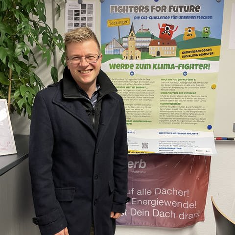 Klimamanager Michael Christ steht in seinem Büro, im Hintergrund ist ein Plakat des Spiels "Fighters for Future" zu sehen.