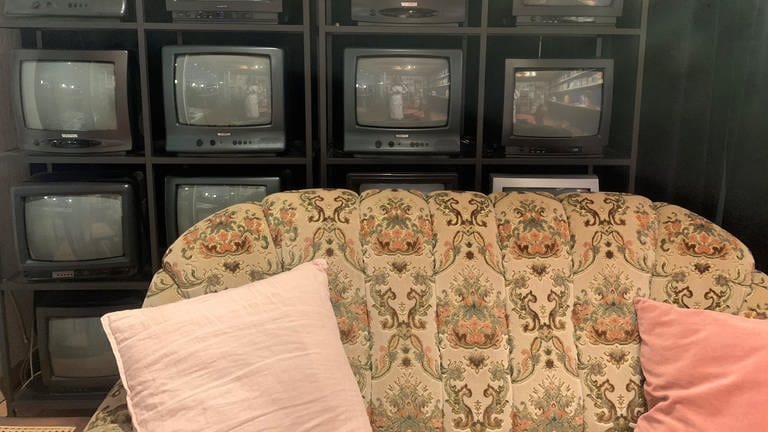 Ein altes Sofa steht vor einer Wand aus alten Fernsehern 