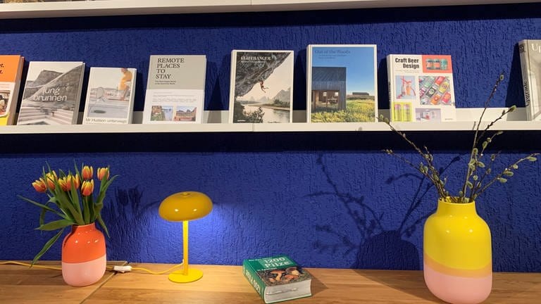 Ein modernes Bücherregal mit einer gelben Lampe vor einen blauen Wand
