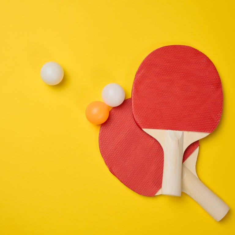 Tischtennisschläger mit drei Tischtennisbällen liegen auf einem gelben Untergrund