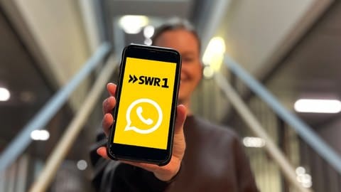 SWR1 Moderatorin Cora Klausnitzer hält ein Smartphone. Darauf zu sehen sind die Logos von SWR1 und Whatsapp.