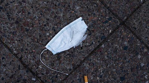 Eine kaputte Coronamaske liegt auf dem Boden. Daneben liegt ein Zigarettenstummel. Je länger die Maske auf dem Boden liegt, desto mehr Mikroplastik und andere Schadstoffe landen im Grundwasser.