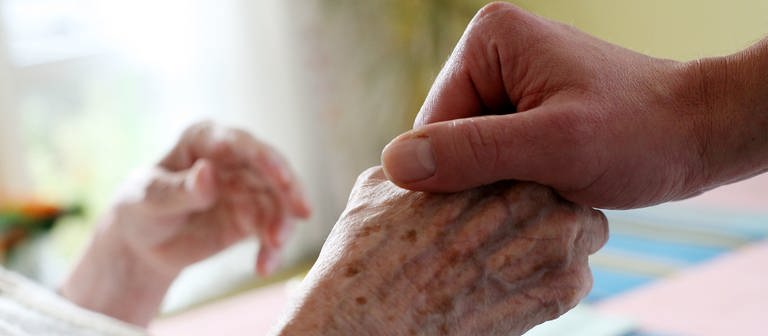Eine pflegende Person hält die Hand eines alten Menschen (Foto: dpa Bildfunk, Picture Alliance)