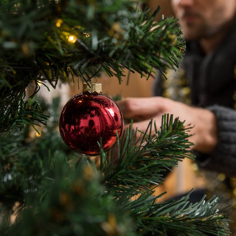 Ein Mann schmückt einen Weihnachtsbaum. (Foto: picture-alliance / Reportdienste, Picture Alliance)