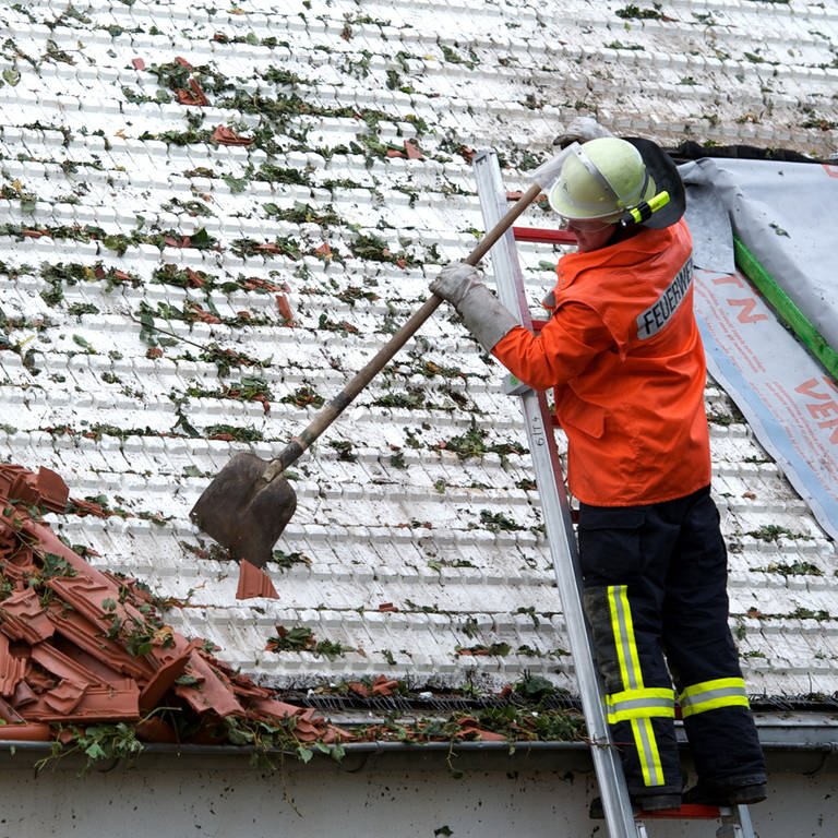 Feuerwehr kehrt Zeigel von kaputtem Dach (Foto: dpa Bildfunk, Peter Endig)