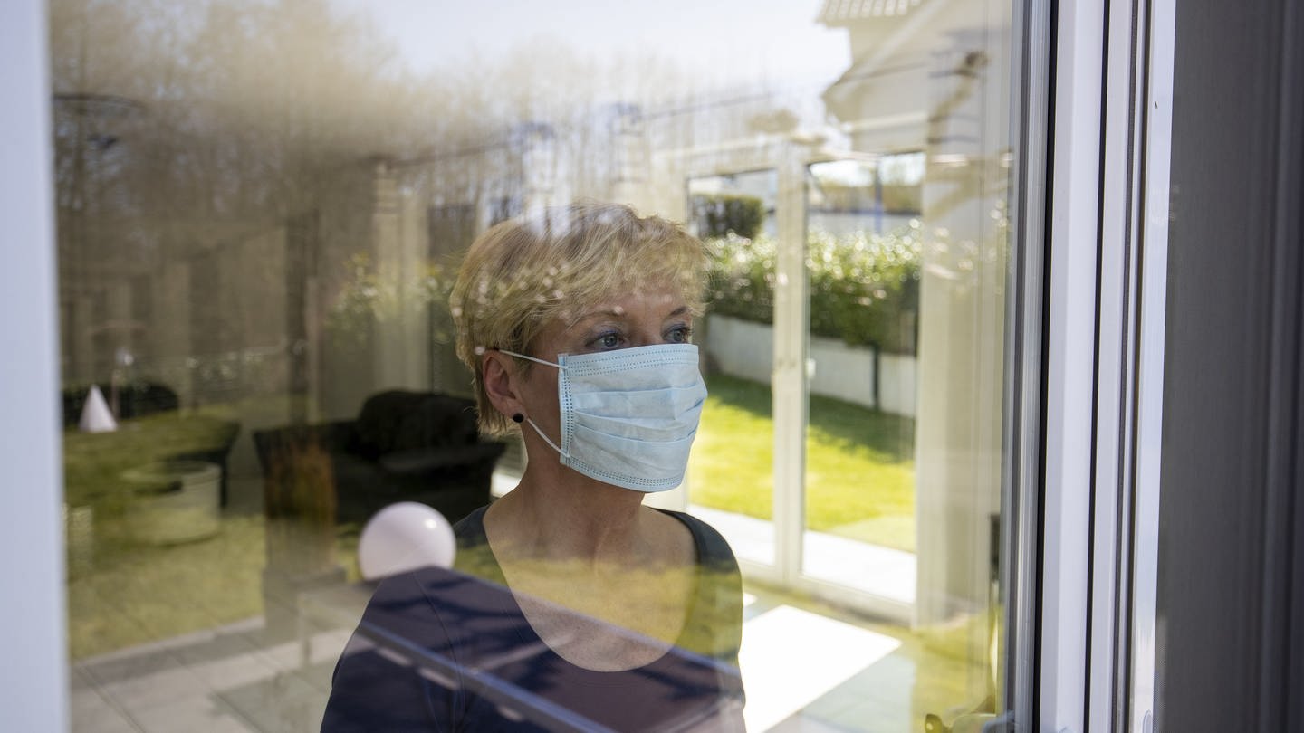 Covid - 19: häusliche Quarantäne Person schaut durch die Scheibe nach draußen mit Mundschutz (Foto: dpa Bildfunk, picture alliance / Joachim Bywaletz)