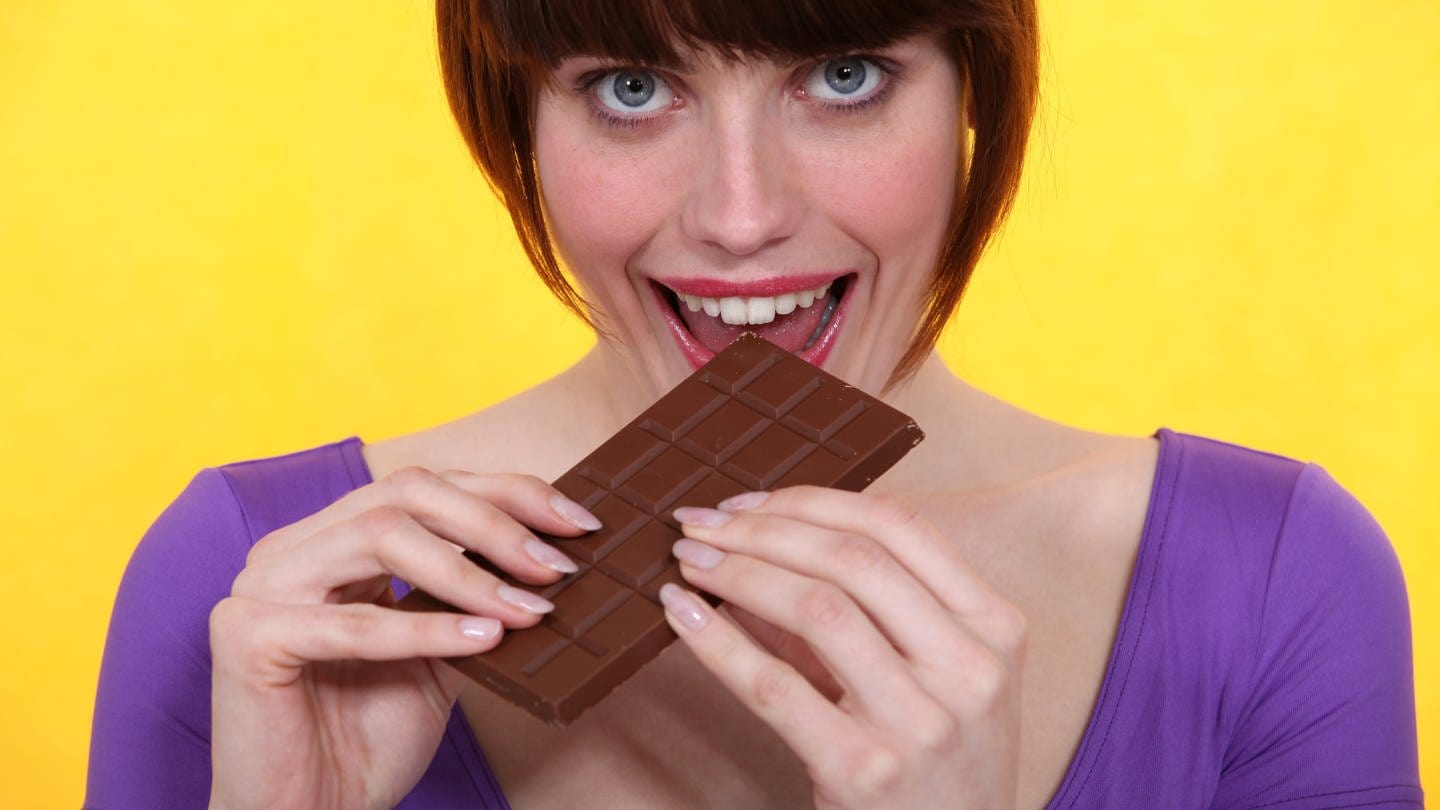 Junge Frau in lila T-Shirt beißt genüssliche in eine Tafel Schokolade