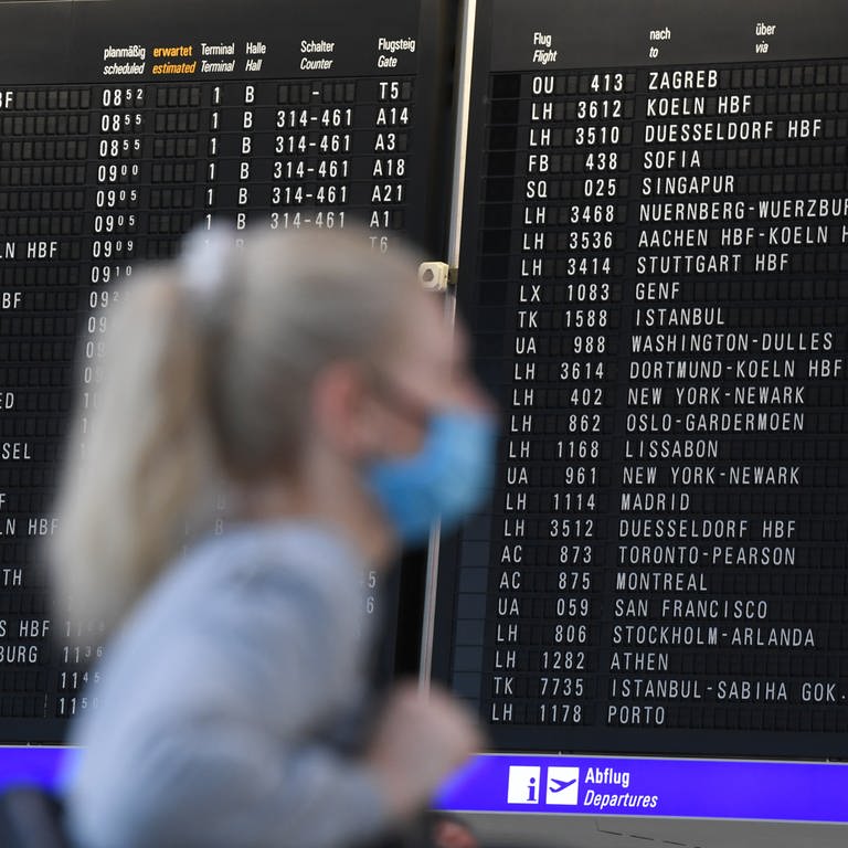  Eine Frau, die einen Mundschutz trägt, steht im Terminal 1 des Frankfurter Flughafens in der Abflughalle vor einer großen Anzeigetafel.