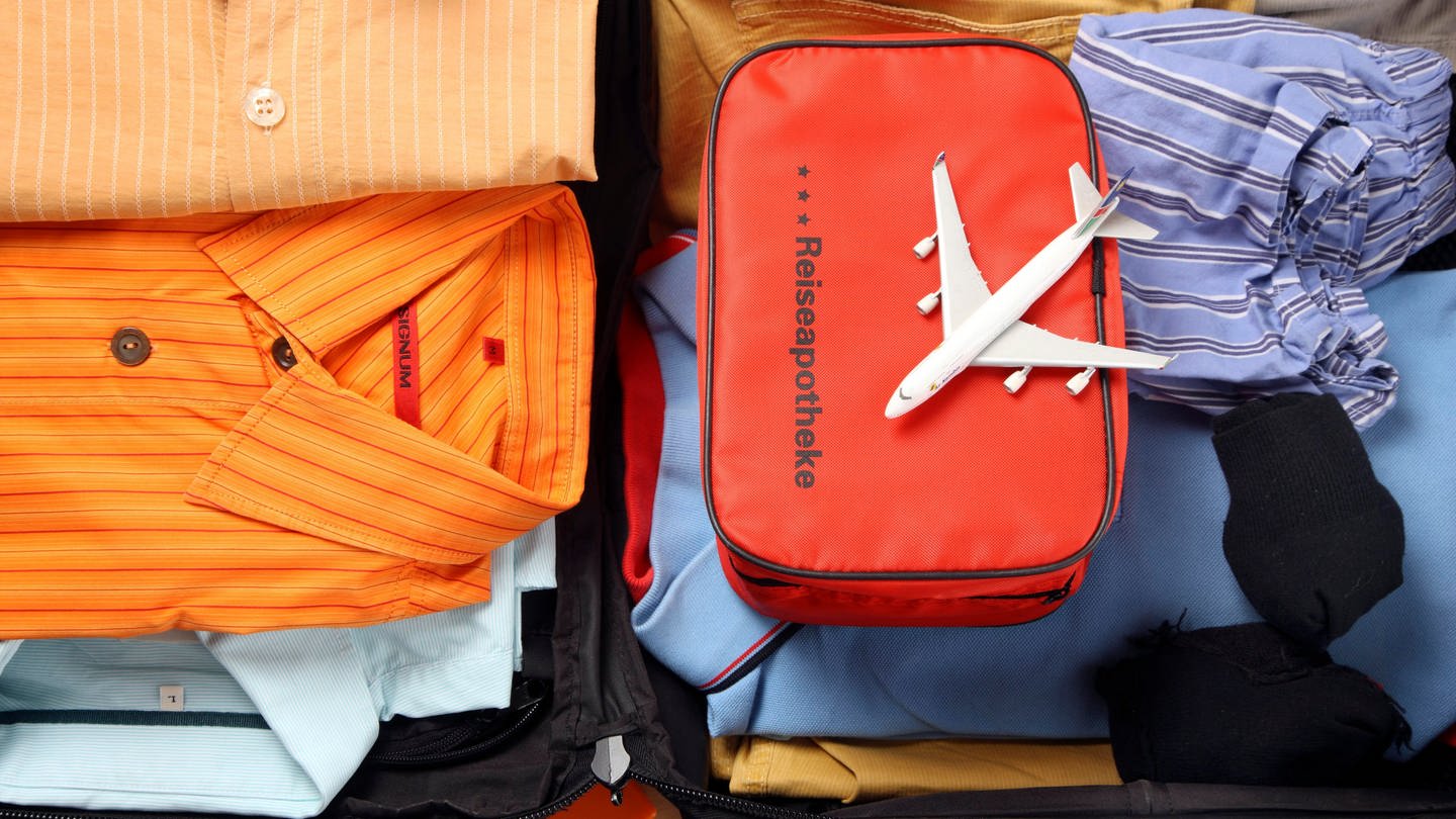 Eine Tasche mit der Aufschrift Reiseapothke liegt in einem gepackten Koffer. Auf ihr befindet sich ein kleines Flugzeug (Foto: picture-alliance / Reportdienste, Picture Alliance)